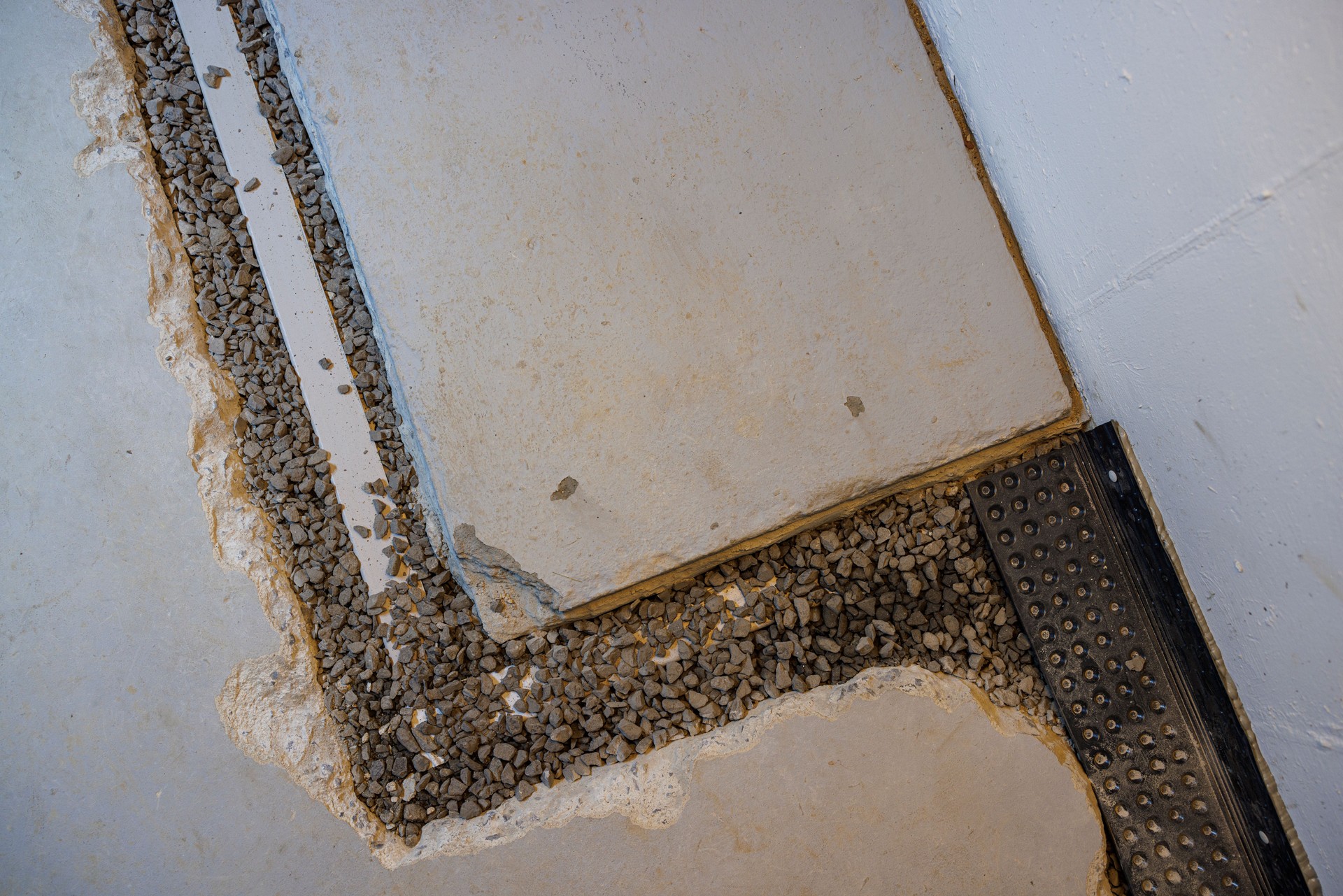 French drain installation. Exposed gravel trench along basement wall with drainage system