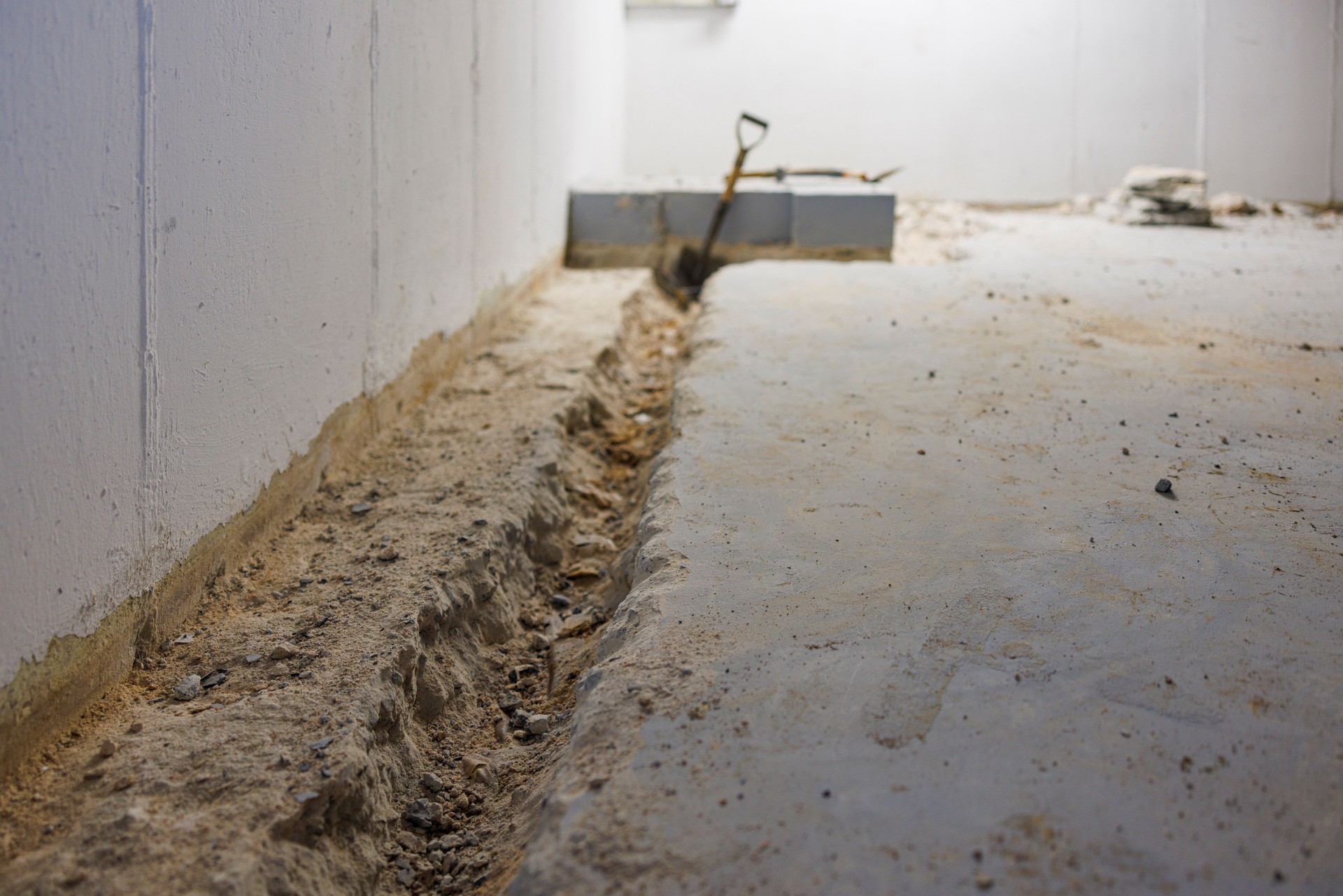 Excavating drainage pathway at residential property. Deep channel carved along interior foundation wall prepares way for water control system